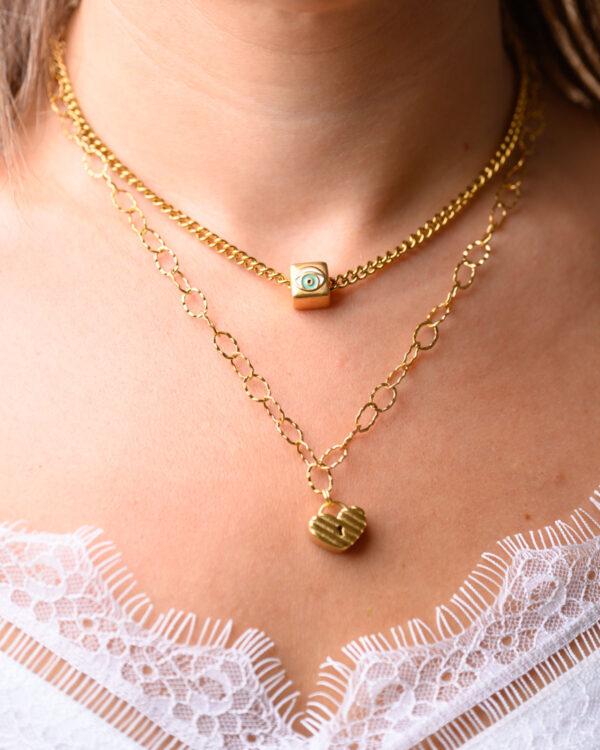 Layered gold necklace set featuring a Cube Eye pendant and a heart locket pendant worn by a woman