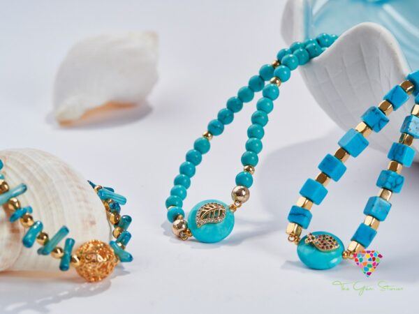 Turquoise beads and cubes necklace with gold elements and fish pendants on a white background with seashells