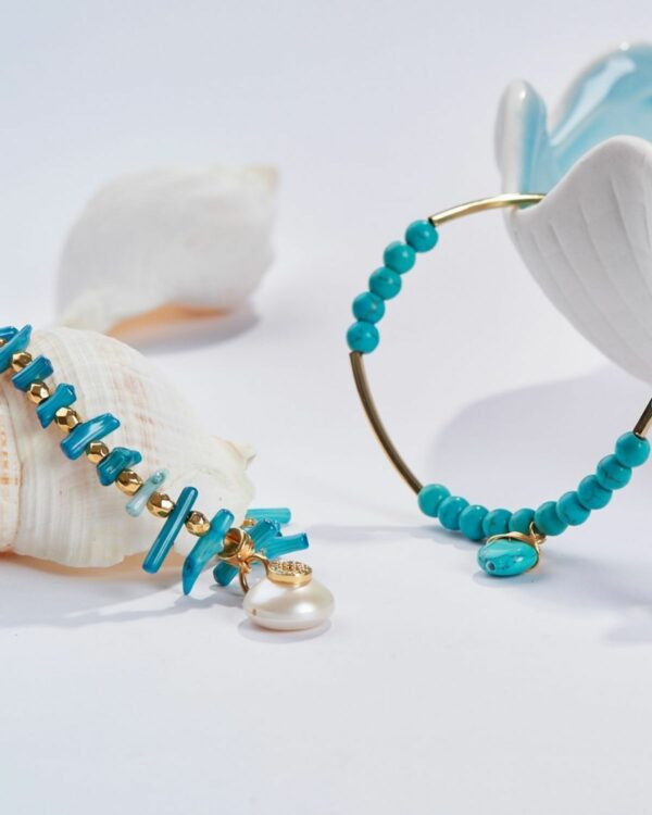 Turquoise jewelry set with gold elements and pearl detail on a white background with seashells and a ceramic dish