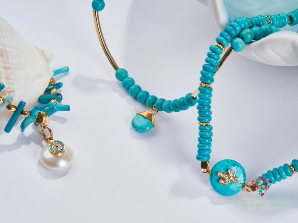 Close-up of turquoise necklace with gold elements and pearl detail on a white background with a ceramic dish