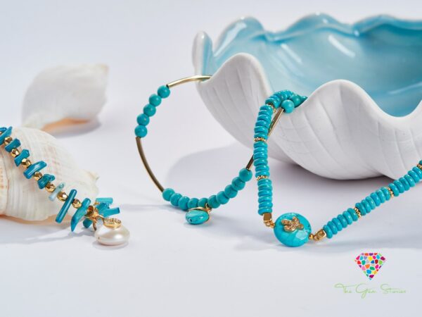 Turquoise necklace with gold elements and pearl detail displayed with seashells and a ceramic dish
