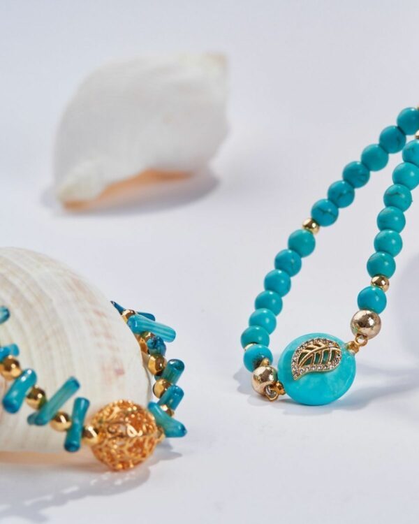 Turquoise rondelle beads necklace with gold elements and cactus pendant on a white background with seashells