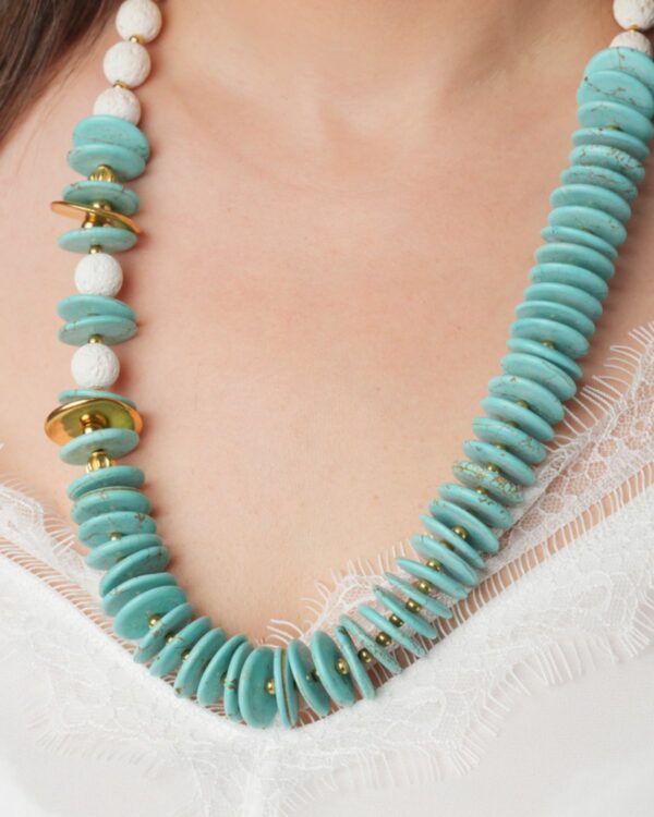 Close-up of a woman wearing a turquoise rondelle and white lava bead necklace with gold accents