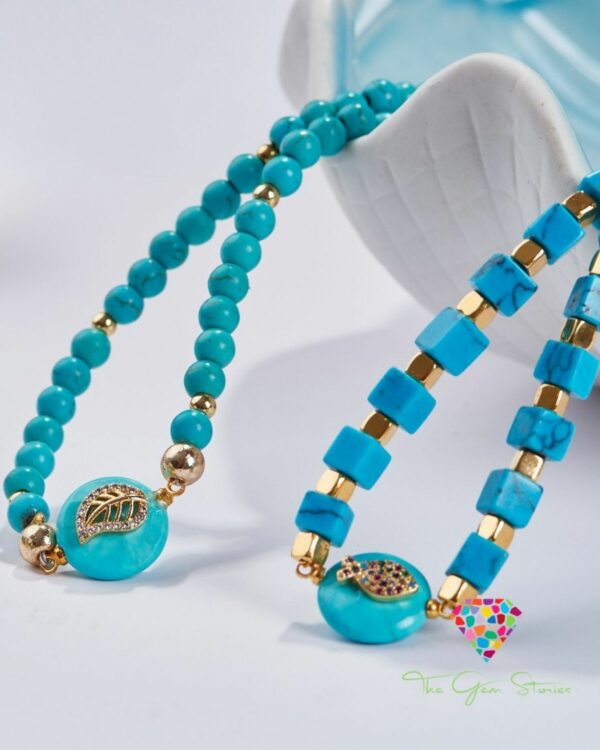 Close-up of two turquoise necklaces featuring leaf elements and gold accents, displayed against a white background