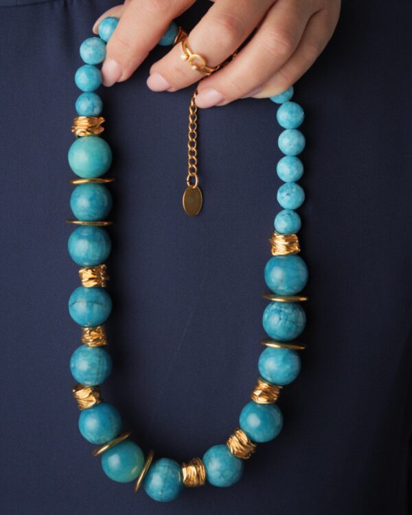 Woman holding a sizeable light blue jade necklace with gold accents