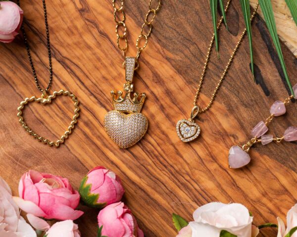Valentine's Day necklace gift ideas, featuring gold and heart-shaped pendants displayed on a wooden background with pink flowers