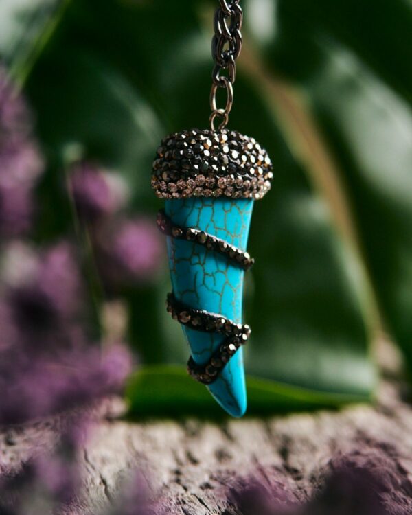 Close-up of a blue howlite tooth pendant with metallic accents on a silver chain