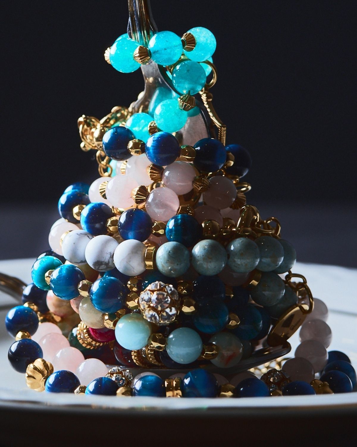 Stack of Gemstone Bracelet Cake featuring vibrant blue, teal, and pink gemstones with golden accents, elegantly arranged on a vintage silver cake stand.