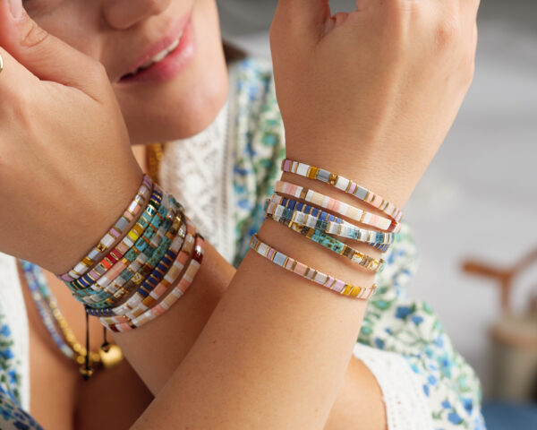 Close-up of a woman wearing multiple colorful Miyuki Tila bracelets on her wrists, featuring intricate beadwork in various patterns and colors