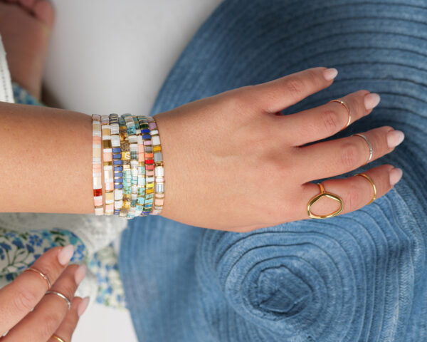 Close-up of a wrist adorned with multiple colorful Miyuki Tila bracelets, displaying intricate beadwork in various patterns and hues