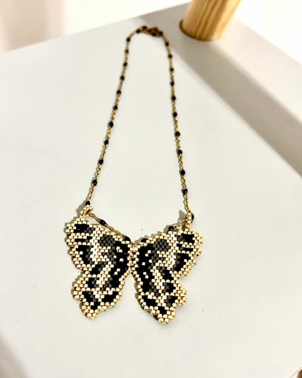 Black and gold Miyuki butterfly necklace displayed on a light surface.