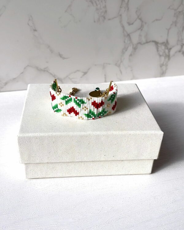 A handcrafted bracelet featuring red and green heart patterns made from Miyuki beads, displayed on a white jewelry box. Perfect holiday accessory or gift idea.