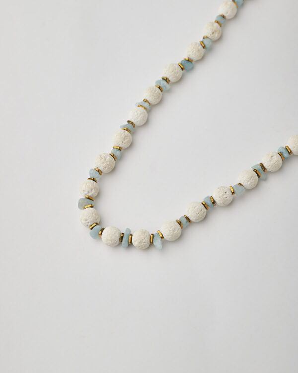 Close-up of handmade white lava and aquamarine necklace with gold spacers and heart charm by The Gem Stories
