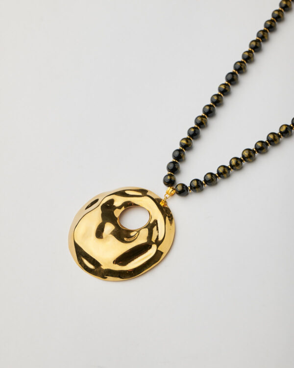 Close-up of gold hammered pendant and black bead strand from handmade necklace