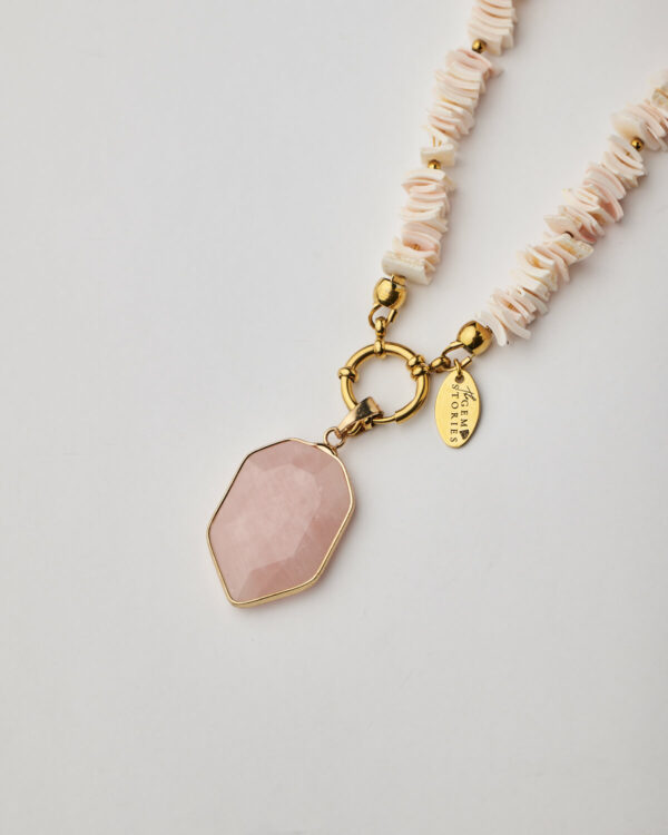 Close-up of faceted rose quartz pendant with gold bezel and shell chips