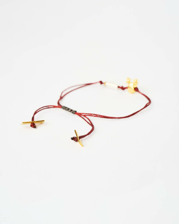 Closeup of the Reindeer Evil Eye Bracelet in red cord with gold reindeer charm and turquoise evil eye bead by The Gem Stories