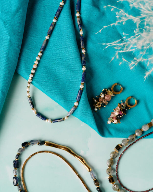 Κολιέ με πολύτιμους λίθους λάπις λάζουλι και μαργαριτάρι με χρυσές λεπτομέρειες, στυλιζαρισμένο πάνω σε τυρκουάζ ύφασμα