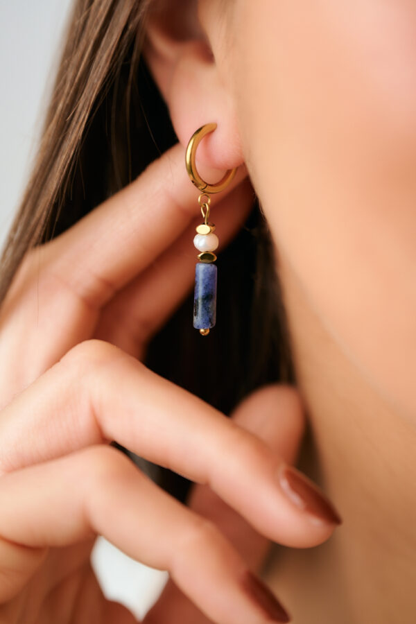 Κοντινή λήψη σκουλαρικιών Λάπις Λάζουλι και μαργαριταριού με χρυσό φορεμένων από μοντέλο του The Gem Stories
