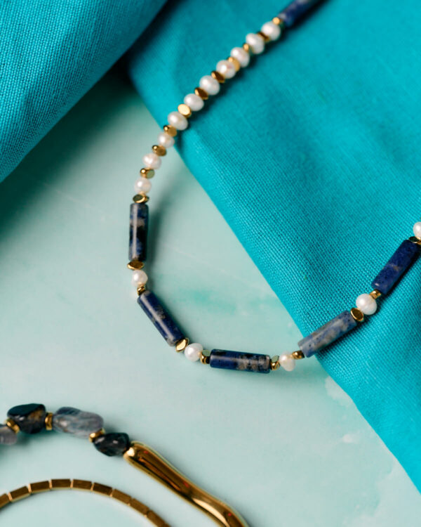 Κοντινή λήψη κολιέ με λάπις λάζουλι και μαργαριτάρι με χρυσές χάντρες διαχωρισμού σε τυρκουάζ φόντο