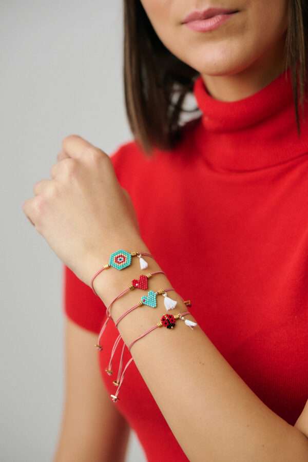 Συλλογή βραχιολιών μαρτάκι φορεμένη από μοντέλο, με κόκκινα κορδόνια και χαντροκοσμημένα μοτίφ, από το The Gem Stories.