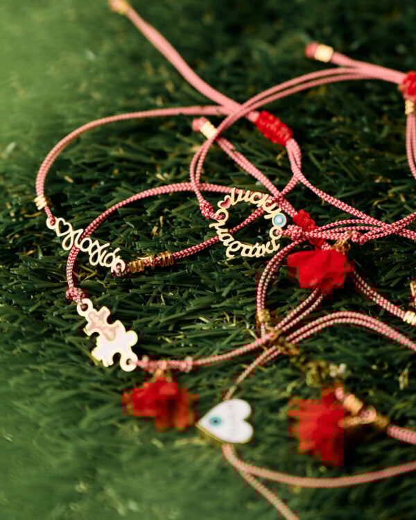 Συλλογή βραχιολιών Μαρτάκι με χρυσά charms σε κόκκινα κορδόνια, τοποθετημένη σε πράσινο φόντο