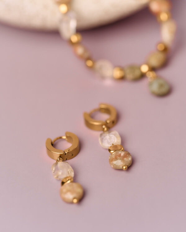 Κοντινή λήψη χρυσών σκουλαρικιών κρίκων με φυσικές πέτρες και κρεμαστές χάντρες από ανάμεικτους πολύτιμους λίθους